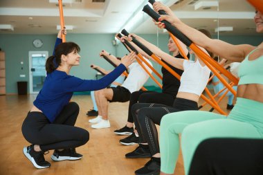Bayan antrenör, spor salonunda jimnastik çubukları kullanarak insanların antrenmanına yardım ediyor. Fitness, spor, eğitim, spor salonu ve yaşam tarzı konsepti