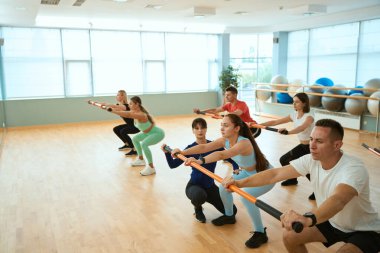 Erkekler ve kadınlar jimnastik kulübünde kadın koçla çömelme hareketleri yapıyorlar. Fitness, spor, eğitim, spor salonu ve yaşam tarzı konsepti