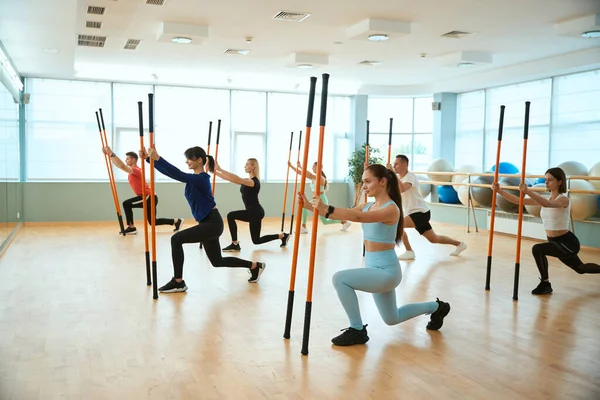 Spor kıyafetli sporcular jimnastik sopasıyla egzersiz yapıyorlar. Fitness, spor, eğitim, spor salonu ve yaşam tarzı konsepti