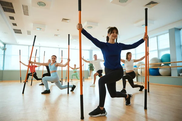 Spor salonunda jimnastik sopalarıyla denge egzersizleri yapan insanlar. Fitness, spor, eğitim, spor salonu ve yaşam tarzı konsepti