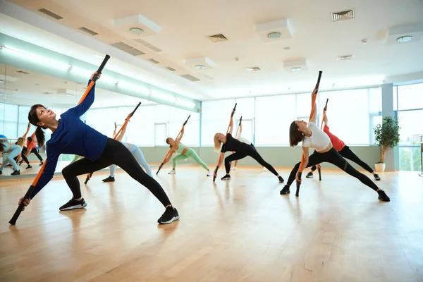 Sportif insanlar jimnastik sopasıyla egzersiz yapıyor, yana doğru eğiliyor. Fitness, spor, eğitim, spor salonu ve yaşam tarzı konsepti