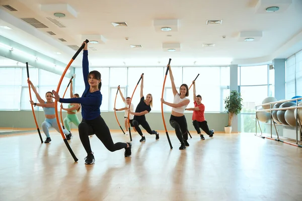 Erkekler ve kadınlar spor salonunda jimnastik sopalarıyla hamleler yapıyorlar. Fitness, spor, eğitim, spor salonu ve yaşam tarzı konsepti