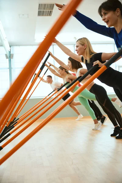 Modern spor salonunda jimnastik sopalarıyla antrenman yapan bir grup insan. Fitness, spor, eğitim, spor salonu ve yaşam tarzı konsepti