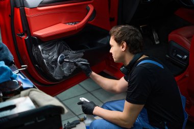 Nitrile eldivenli oto temizleyici fırça ve otomotiv sabunu ile arabanın iç kapağını temizliyor.