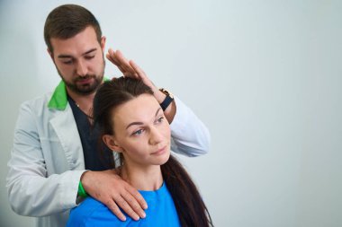 Beyaz laboratuvar önlüklü bir adam, bir tıp odasında kadınları baştan aşağı inceliyor. Kadın terapi sırasında sakin ve düşünceli görünüyor..