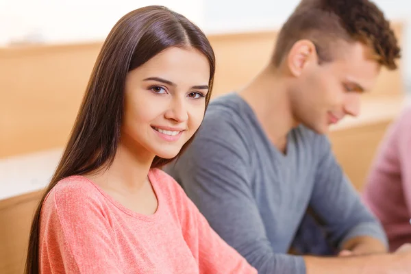 Joven chica sonriente está sentada en el escritorio . — Foto de Stock