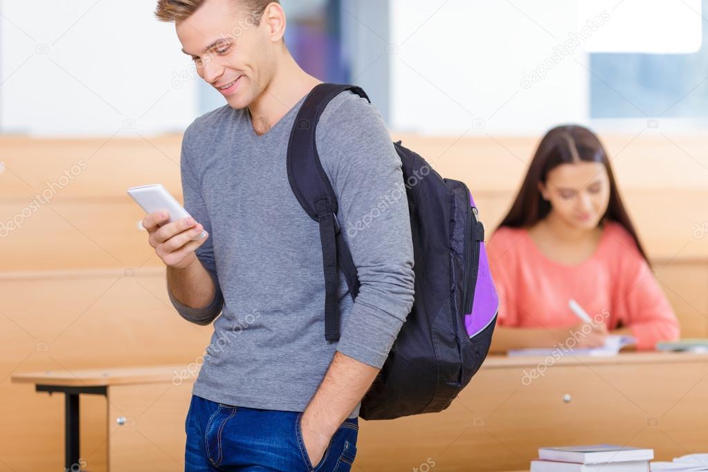 Smiling student is texting on the phone.