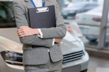 Saleswoman with clipboard is standing beside the car.