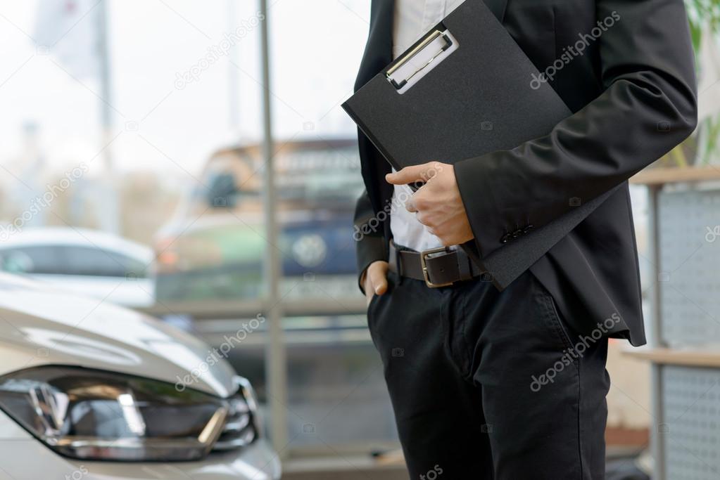 Salesman with clipboard is standing beside the car.