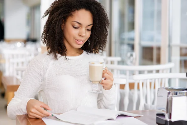 Mujer atractiva leyendo una revista mientras bebe café . — Foto de Stock