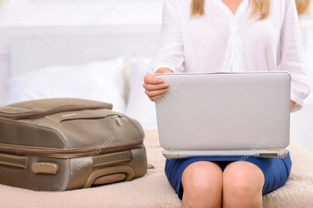 Hotel resident sitting on bed and using laptop.