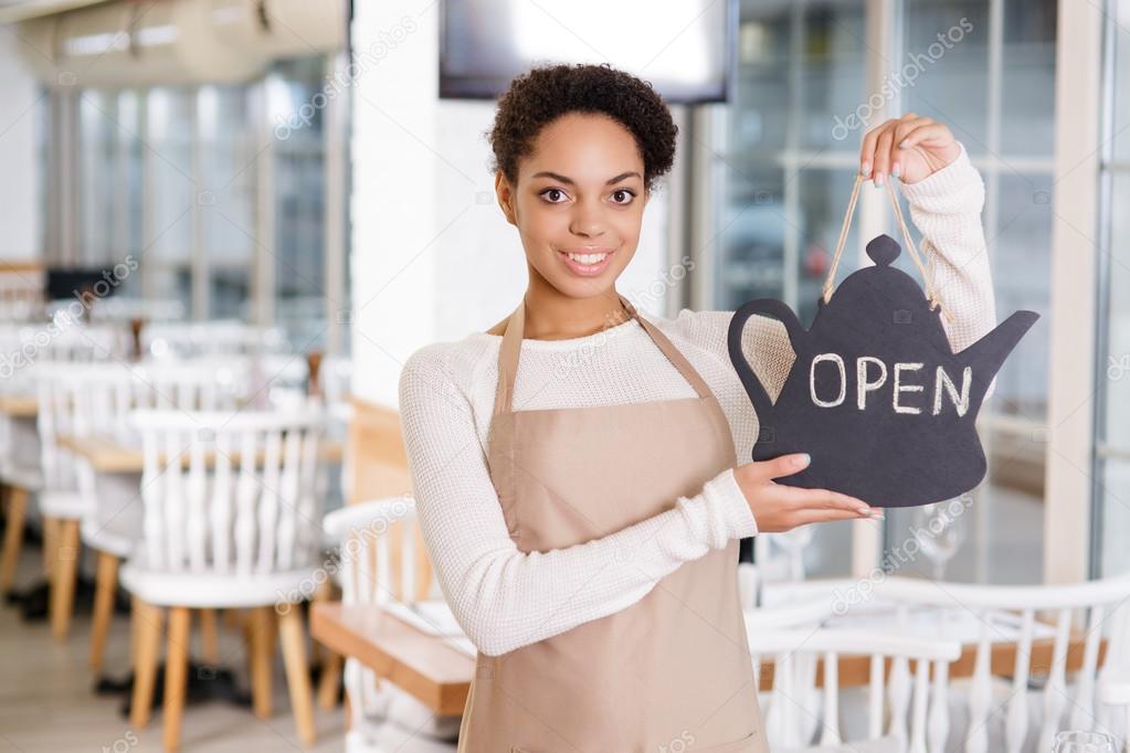 Smiling waitress holding an opening sign.