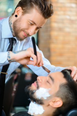 Professional barber shaving the beard of his client