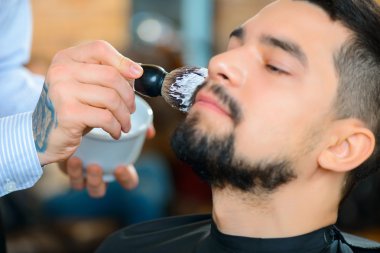 Professional barber shaving the beard of his client