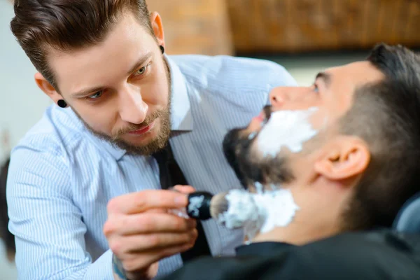 Barbeiro profissional barbeando a barba de seu cliente — Fotografia de Stock