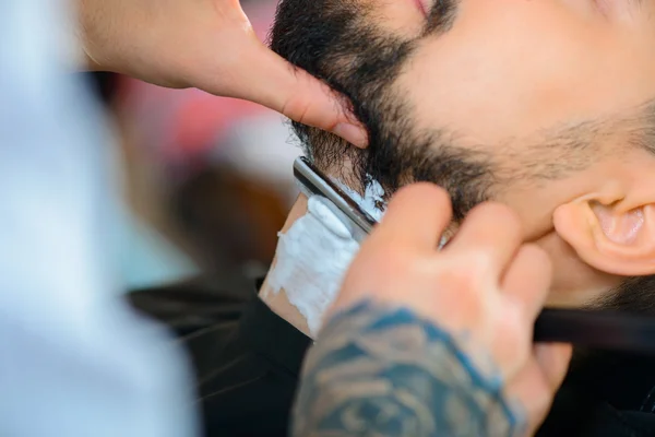 Barbeiro profissional barbeando a barba de seu cliente — Fotografia de Stock