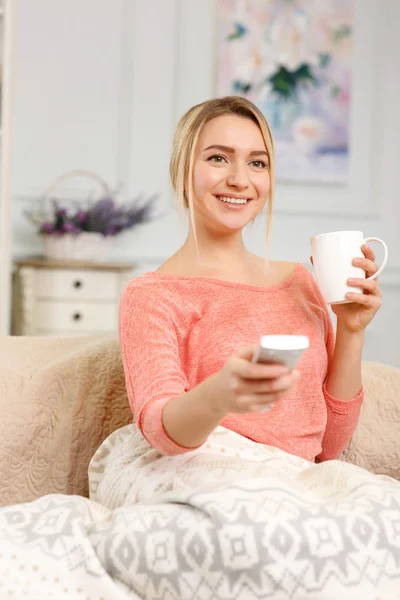 Joven mujer sonriente viendo la televisión en el sofá . — Foto de Stock