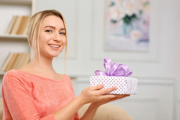 Młoda kobieta uśmiechający się jest podtrzymywanie owinięty prezent. — Zdjęcie stockowe