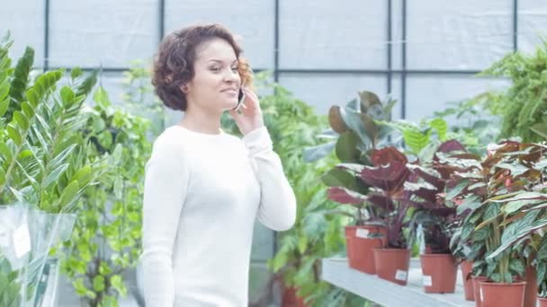 Jonge vrouw met een telefoon praten in de serre. — Stockvideo