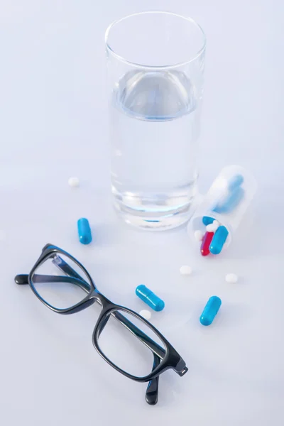 Vidro de água, comprimidos e óculos — Fotografia de Stock