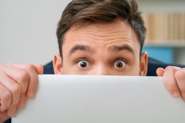 Pleasant office worker hiding behind laptop