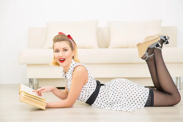 Schöne junge Frau liest, während sie auf dem Boden liegt. — Stockfoto