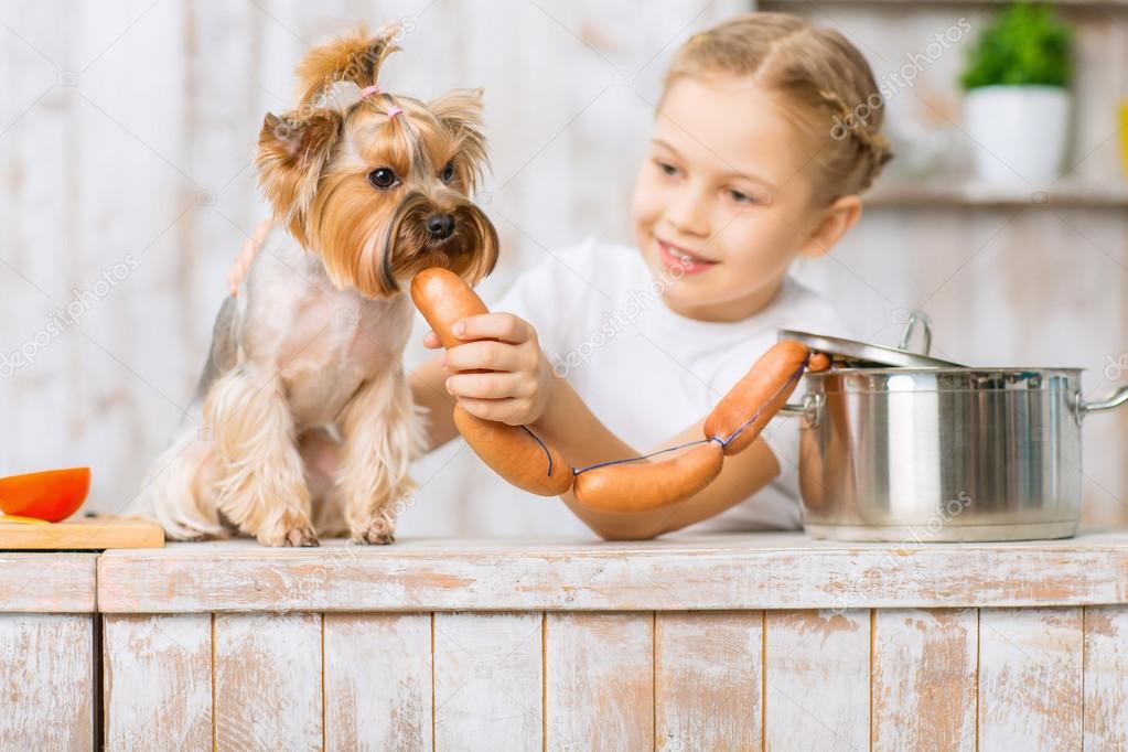 Little girl is feeding sausages to her dog.