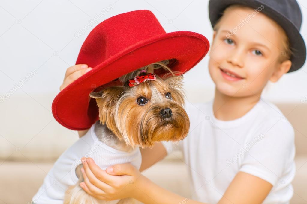 Little girl is putting red hat on her dog.