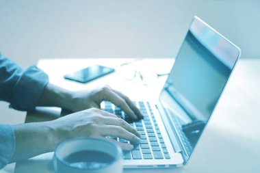 Sıradan bir iş adamı elinde bir fincan kahveyle dizüstü bilgisayarda çalışıyor..