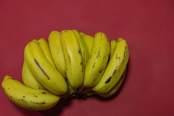 Bunch of yellow bananas. Bananas on the red background. Exotic fruit rich in fiber and source of potassium. Banana fruit (Musa spp.). Plant typical of humid tropical regions.