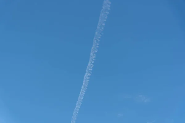 Blue sky cut by smoke from airplane fuel. Aviation kerosene waste. Aircraft fuel trail on the horizon. Environment pollution. Commercial aviation.