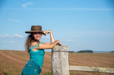 Kırsal arazi çitlerine asılmış bir şapka takan Brezilyalı kadın. Yaşam tarzı. Brezilya 'da çiftlik bölgesinde poz veren bir kız. Kırsal alan.