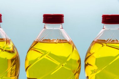Mavi arka planda yenilebilir soya yağı olan plastik şişeler. Bitkisel yağ. Soya yağı, soya fasulyesinden elde edilen ve doymamış yağ, omega 3 ve 6 ve E vitamini bakımından zengin bir sebze yağı türüdür..
