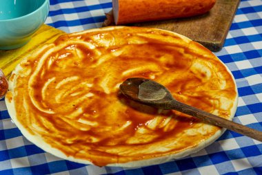 Tahta kaşığın üzerine tarantella soslu pizza hamuru yayılıyor. İtalyan mutfağı. Mutfak lezzeti. Pizza üretimi için buğday hamuruna sürülmüş kırmızı sos..
