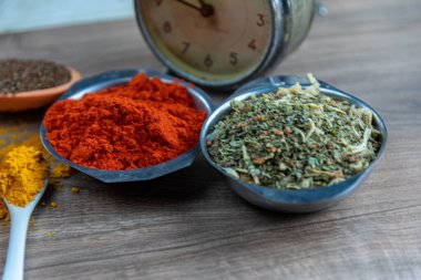 Renkli mutfak baharatları ve ahşap yüzeydeki saat. Yemek pişirmek için kullanılan malzemeler. Yemek masasındaki analog saat. Baharatlar aromalı gıdaya.