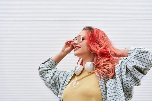 Mladá hipsterová žena s barveným růžovým účesem, bezdrátovými sluchátky a slunečními brýlemi s úsměvem — Stock fotografie