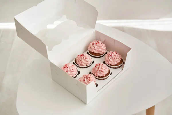 白いテーブルの上のギフトボックスにピンクのカップケーキ. — ストック写真
