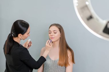 Makyaj sanatçısı mavi gözlü kadına makyaj yapıyor fırça ve göz farıyla.