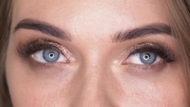 Makyöz, mavi gözlü kadına fırça ve göz farı kullanarak makyaj yapıyor.