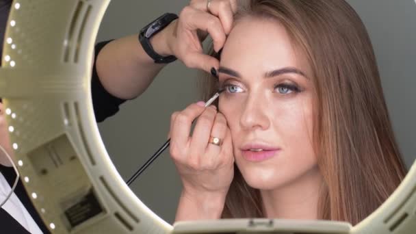 Make-up artist gör makeup till kvinnan med blå ögon med pensel och ögonskugga — Stockvideo