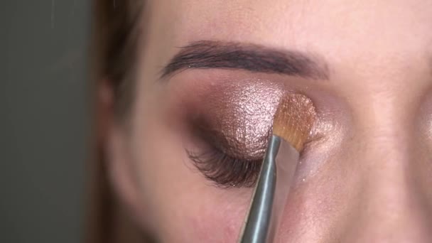 Make-up artist gör makeup till kvinnan med blå ögon med pensel och ögonskuggor — Stockvideo