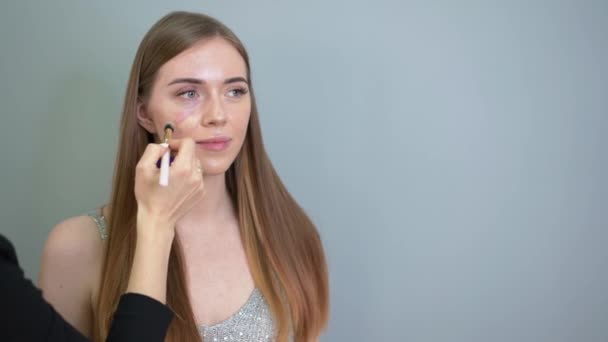 Make-up kunstenaar aanbrengen stichting op het gezicht van een vrouw door borstel. Salon — Stockvideo