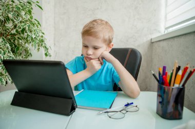 Genç çocuk evde tabletle öğreniyor. Karantinada uzaktan öğrenme. İzolasyon. Ev ödevi
