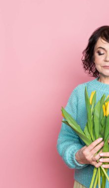 Profesyonel dumanlı makyajlı ve elinde pembe arka planda lale çiçekleri tutan güzel bir kadın.