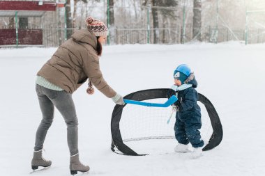 Annesiyle parkta paten kayan komik çocuk. Sopa ve golle buz hokeyi oynamak. Açık havada. Kış sporu