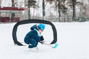 Annesiyle parkta paten kayan komik çocuk. Sopa ve golle buz hokeyi oynamak. Açık havada. Kış sporu
