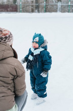 Küçük komik çocuk annesiyle parkta paten kaymayı öğreniyor. Açık havada. Kış sporu