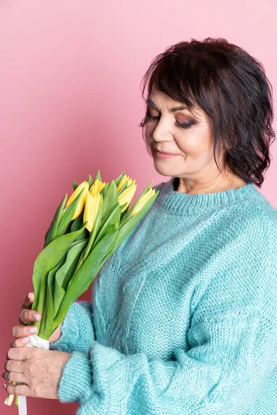 Mulher velha bonita com maquiagem profissional e penteado segurando flores de tulipa no fundo rosa — Fotografia de Stock