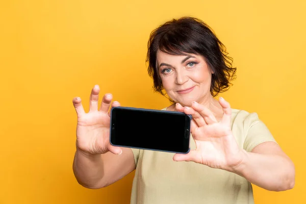美しいですシニア女性作る自撮りによってスマートフォン上の黄色の背景 — ストック写真