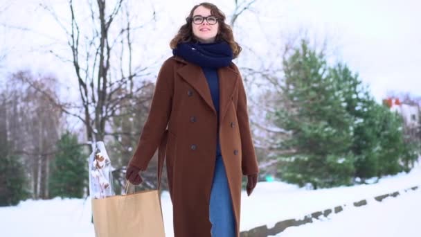Junge schöne Frau mit Strickschal steht mit Einkaufstasche im Park — Stockvideo